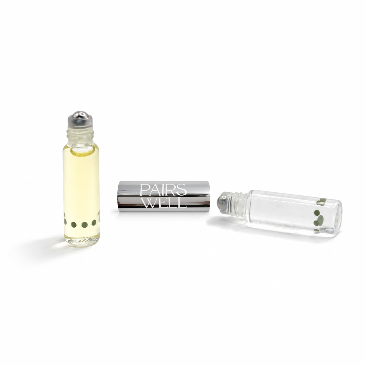 Two glass bottles with metal roller ball applicators. One with yellow fragrance and one with clear lip serum. Metal connector piece separately in the middle of the two bottles